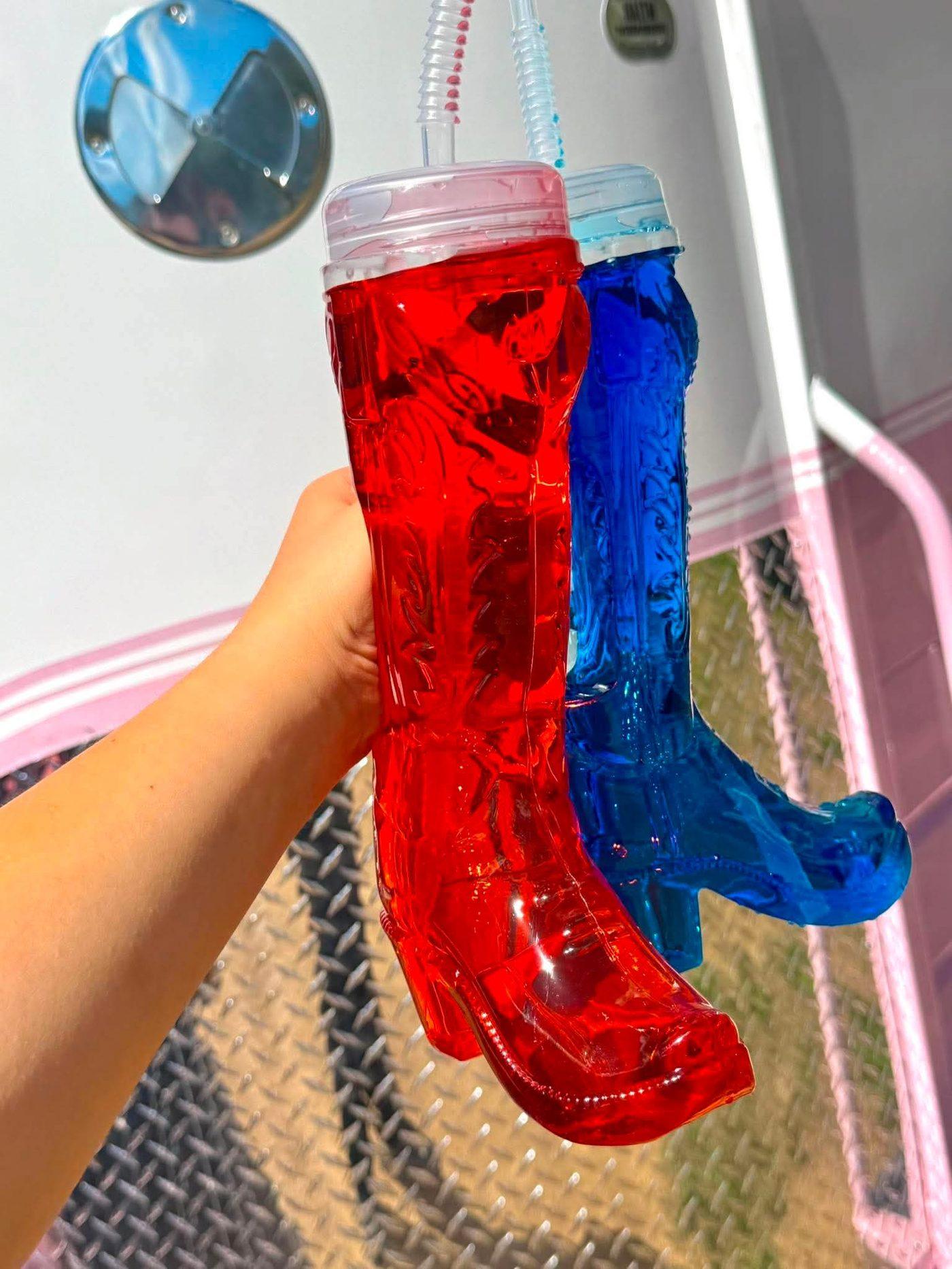 A hand holding two cowboy boot cups, one red and one blue