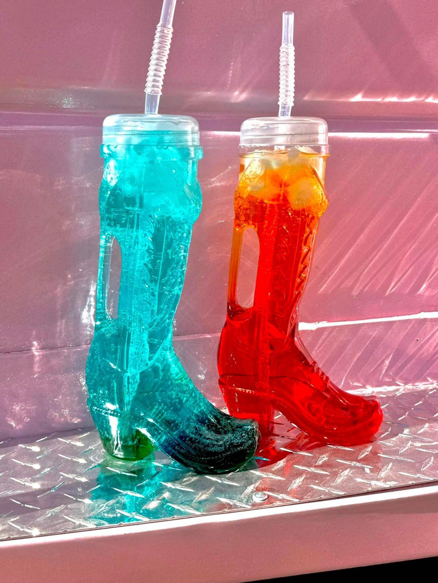 Two cowboy boot cups, one filled with teal blue raspberry soda, one with red cherry soda