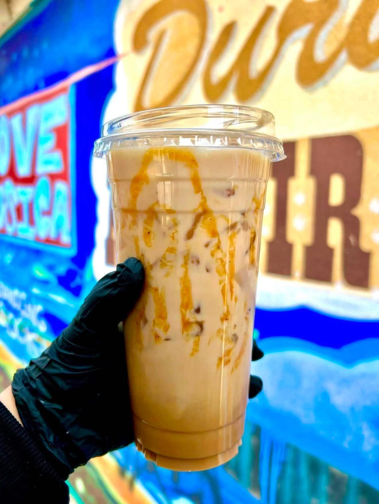 Iced coffee drink with caramel drizzle held in front of a colorful mural