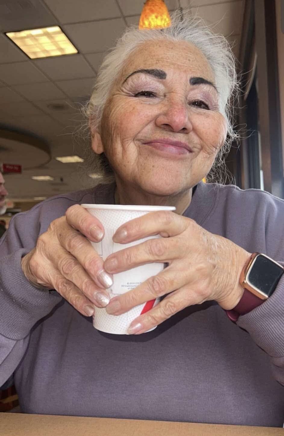 The founder's grandmother smiling and holding a coffee cup — the real woman behind She'Brews